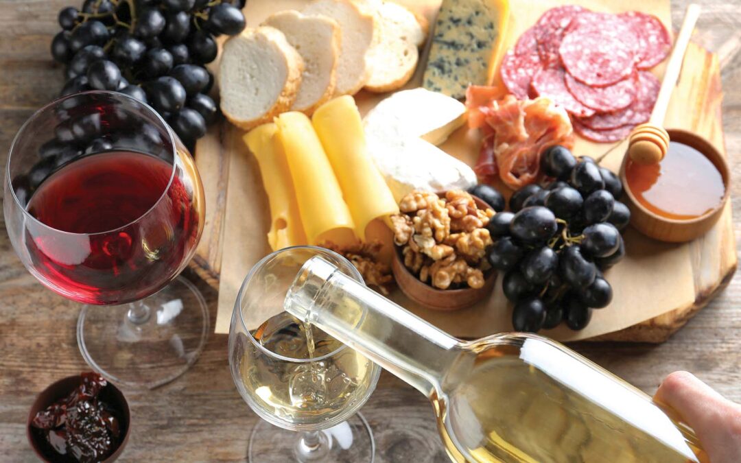 Woman pouring white wine into glass on table with delicious food