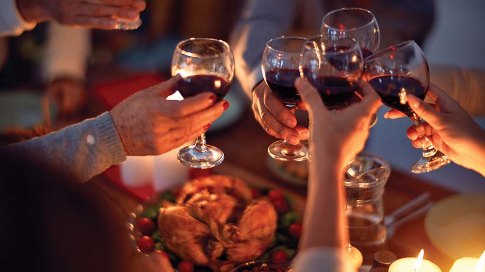 Family and friends dining at home celebrating christmas eve with traditional food and decoration, all sitting on the table together making a toast