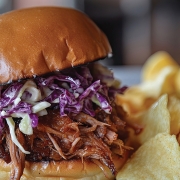 A pulled pork sandwich with coleslaw on a brioche bun, served wi